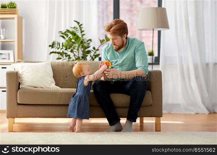 family, fatherhood and people concept - happy red haired father with ball playing with little baby daughter at home. father playing with little baby daughter at home. father playing with little baby daughter at home