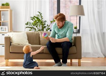 family, fatherhood and people concept - happy red haired father with ball playing with little baby daughter at home. father playing with little baby daughter at home