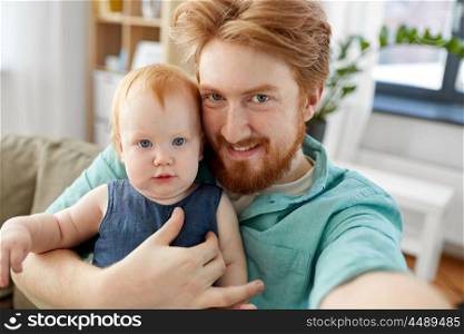 family, fatherhood and people concept - happy red haired father with little baby daughter taking selfie at home. happy father with baby taking selfie at home. happy father with baby taking selfie at home