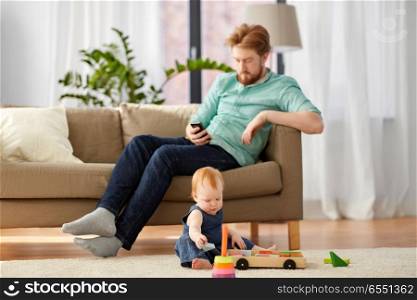 family, fatherhood and people concept - happy red haired father with smartphone and little baby daughter playing with toy blocks kit at home. father and baby playing with toy blocks at home. father and baby playing with toy blocks at home
