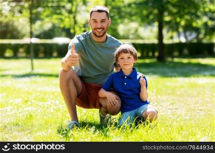 family, fatherhood and people concept - happy smiling father showing thumbs up with little son at summer park. happy smiling father and little son at summer park