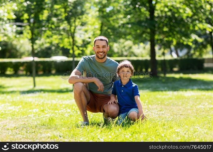 family, fatherhood and people concept - happy smiling father with little son at summer park. happy smiling father and little son at summer park