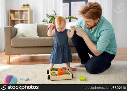 family, fatherhood and people concept - red haired little baby girl standing with father help at home. baby girl standing with father help at home