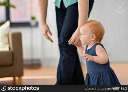 family, fatherhood and people concept - red haired little baby girl walking with father help at home. baby girl walking with father help at home. baby girl walking with father help at home