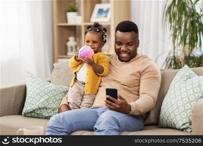 family, fatherhood and technology concept - african american father with smartphone and little baby daughter playing with ball at home. father with smartphone and baby daugter at home