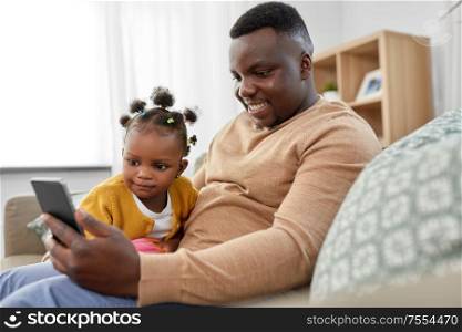 family, fatherhood and technology concept - african american father with smartphone and little baby daughter playing with ball at home. father with smartphone and baby daughter at home