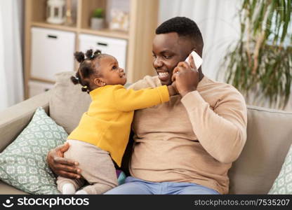 family, fatherhood and technology concept - happy african american father with baby at home calling on smartphone. father with baby at home calling on smartphone