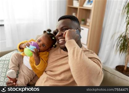 family, fatherhood and technology concept - happy african american father with baby at home calling on smartphone. father with baby at home calling on smartphone