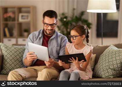 family, fatherhood and technology concept - happy father and daughter in glasses with tablet pc computers at home. father and daughter with tablet computers at home