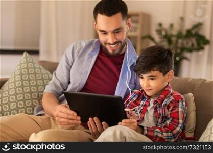 family, fatherhood and technology concept - happy father and little son with tablet pc computer and earphones listening to music at home. father and son listening to music on tablet pc