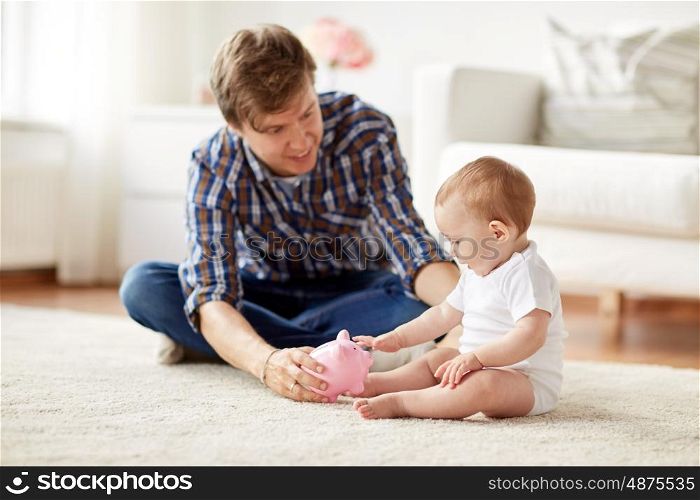 family, fatherhood, finances and parenthood concept - happy smiling young father and little baby playing with piggy bank at home