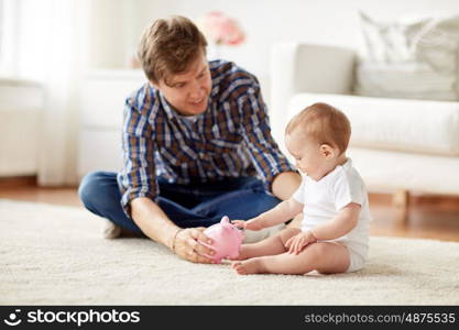 family, fatherhood, finances and parenthood concept - happy smiling young father and little baby playing with piggy bank at home