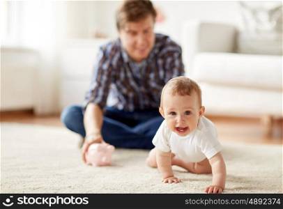 family, fatherhood, finances and parenthood concept - happy smiling young father and little baby playing with piggy bank at home
