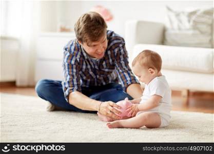 family, fatherhood, finances and parenthood concept - happy smiling young father and little baby playing with piggy bank at home. happy father with baby and piggy bank at home