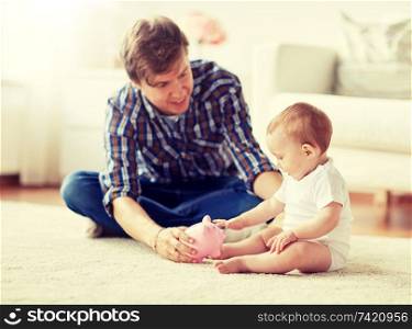 family, fatherhood, finances and parenthood concept - happy smiling young father and little baby playing with piggy bank at home. happy father with baby and piggy bank at home