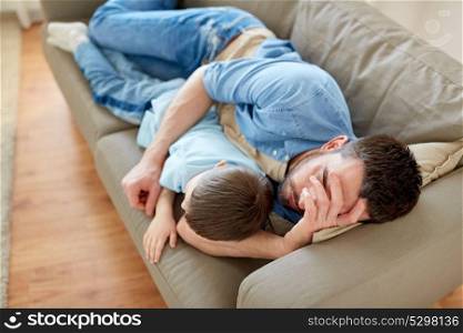 family, fatherhood, leisure and people concept - father and little son sleeping on sofa at home. father and son sleeping on sofa at home