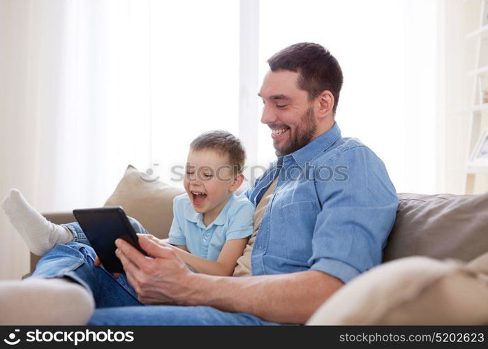 family, fatherhood, technology and people concept - happy father and little son with tablet pc computer sitting on sofa at home. father and son with tablet pc playing at home