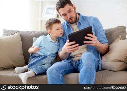 family, fatherhood, technology and people concept - happy father and little son with tablet pc computer sitting on sofa at home. father and son with tablet pc playing at home