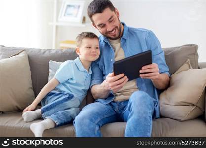 family, fatherhood, technology and people concept - happy father and little son with tablet pc computer sitting on sofa at home. father and son with tablet pc playing at home