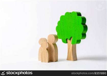 Family figures are standing near the tree. Pastime with family, kinship and parenting. Instilling good qualities and values in a healthy society. The concept of happiness and unity with nature. Health
