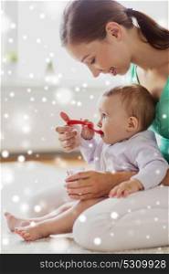 family, food and parenthood concept - happy mother with spoon feeding little baby eating puree at home over snow. mother with spoon feeding little baby at home