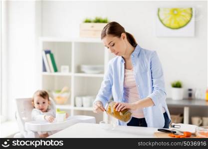 family, food, child, eating and parenthood concept - mother with blender cooking puree for her baby sitting in highchair at home kitchen. mother with blender cooking baby food at home