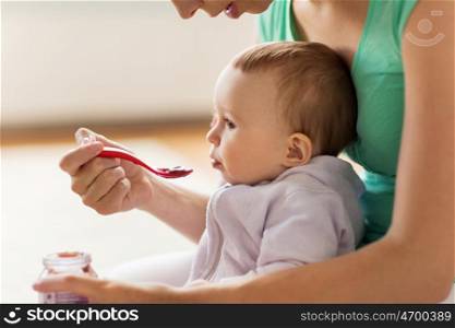family, food, child, eating and parenthood concept - mother with puree and spoon feeding little baby at home
