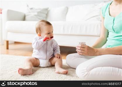 family, food, child, feeding and parenthood concept - mother and baby with spoon eating puree from jar at home