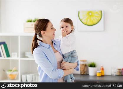 family, food, eating, motherhood and people concept- happy mother and little baby girl at home kitchen. happy mother and little baby girl at home kitchen