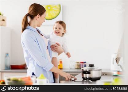 family, food, healthy eating and people concept - happy mother and little baby girl cooking dinner together at home kitchen. happy mother and baby cooking at home kitchen
