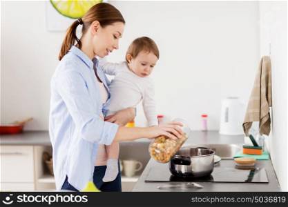family, food, healthy eating and people concept - happy mother and little baby girl cooking pasta for dinner together at home kitchen. mother and baby cooking pasta at home kitchen