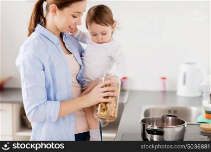 family, food, healthy eating and people concept - happy mother and little baby girl cooking pasta for dinner together at home kitchen. mother and baby cooking pasta at home kitchen