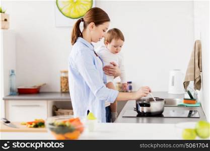 family, food, healthy eating and people concept - happy mother and little baby girl cooking dinner together at home kitchen. happy mother and baby cooking at home kitchen