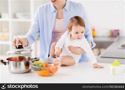 family, food, healthy eating, cooking and people concept - happy mother and little baby girl with vegetables and pot at home kitchen. happy mother and baby cooking vegetables at home