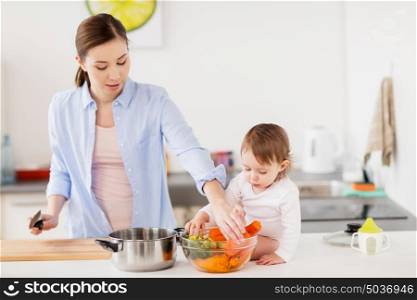 family, food, healthy eating, cooking and people concept - happy mother and little baby girl with vegetables and pot at home kitchen. happy mother and baby cooking food at home kitchen