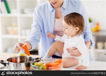 family, food, healthy eating, cooking and people concept - happy mother and little baby girl with vegetables and pot at home kitchen. happy mother and baby cooking vegetables at home