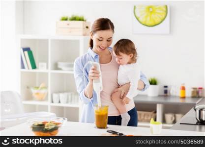 family, food, healthy eating, cooking and people concept - happy mother with blender blending vegetable puree and little baby girl with at home kitchen. happy mother and baby cooking food at home kitchen