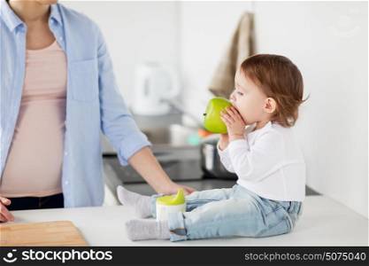 family, food, healthy eating, people and motherhood concept - mother and baby with green apple at home kitchen. mother and baby eating green apple at home kitchen