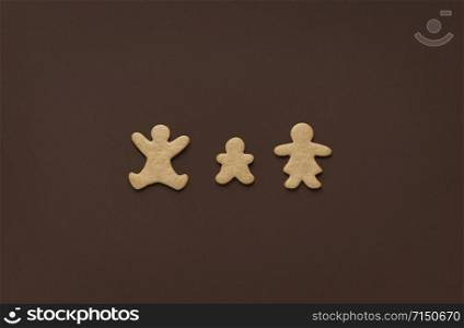 Family for Christmas concept with gingerbread cookies in shape of parents and child, minimal, on a brown background. Above view of Christmas sweets.