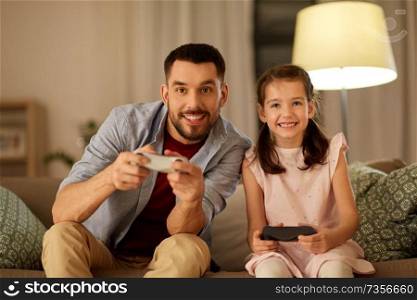 family, gaming and entertainment concept - happy father and little daughter with gamepads playing video game at home in evening. father and daughter playing video game at home