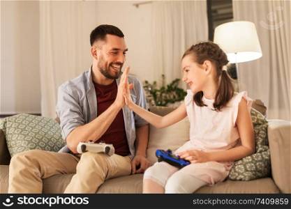 family, gaming and entertainment concept - happy father and little daughter with gamepads playing video game at home. father and daughter playing video game at home