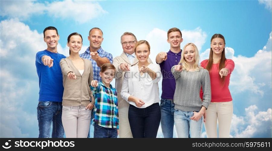 family, gender, generation and gesture concept - group of happy people pointing finger on you over blue sky and clouds background