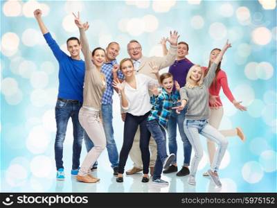 family, gender, generation and people concept - group of smiling men, women and boy having fun and waving hands over blue holidays lights background