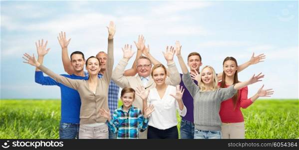family, gender, generation and people concept - group of smiling men, women and boy waving hands over blue sky and grass background