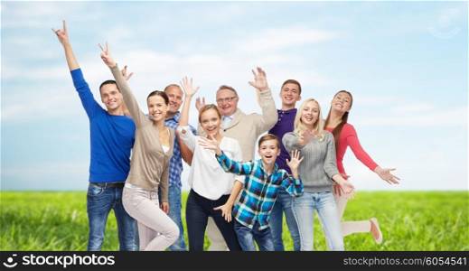 family, gender, generation and people concept - group of smiling men, women and boy having fun and waving hands over blue sky and grass background