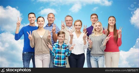 family, gender, victory and people concept - group of smiling men, women and boy showing peace hand sign over blue sky and clouds background