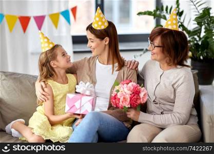 family, generation and celebration concept - smiling daughter with gift box and grandmother with flowers greeting mother on birthday at home. daughter with gift box greeting mother on birthday