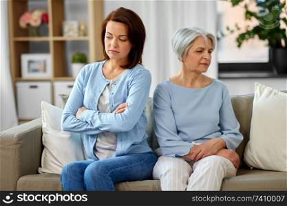 family, generation and disagreement concept - upset senior mother and adult daughter sitting on sofa at home. disagreement between senior mother adult daughter