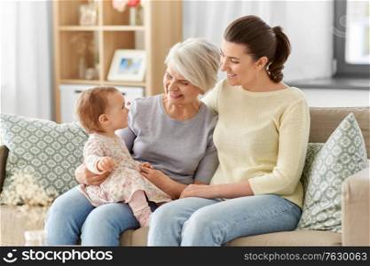 family, generation and female concept - happy smiling mother, baby daughter and grandmother sitting on sofa at home. mother, daughter and grandmother on sofa at home