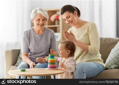 family, generation and female concept - happy smiling mother, baby daughter and grandmother playing with toy pyramid at home. mother, baby daughter and granny playing at home